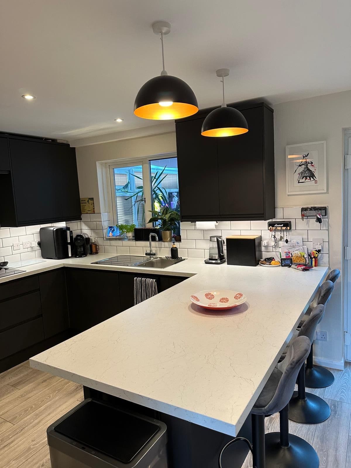 Kitchen with black handleless cabinetry, white marble effect worktop breakfast bar, black dome pendant lights and grey upholstered bar stools, Pennyland, Milton Keynes