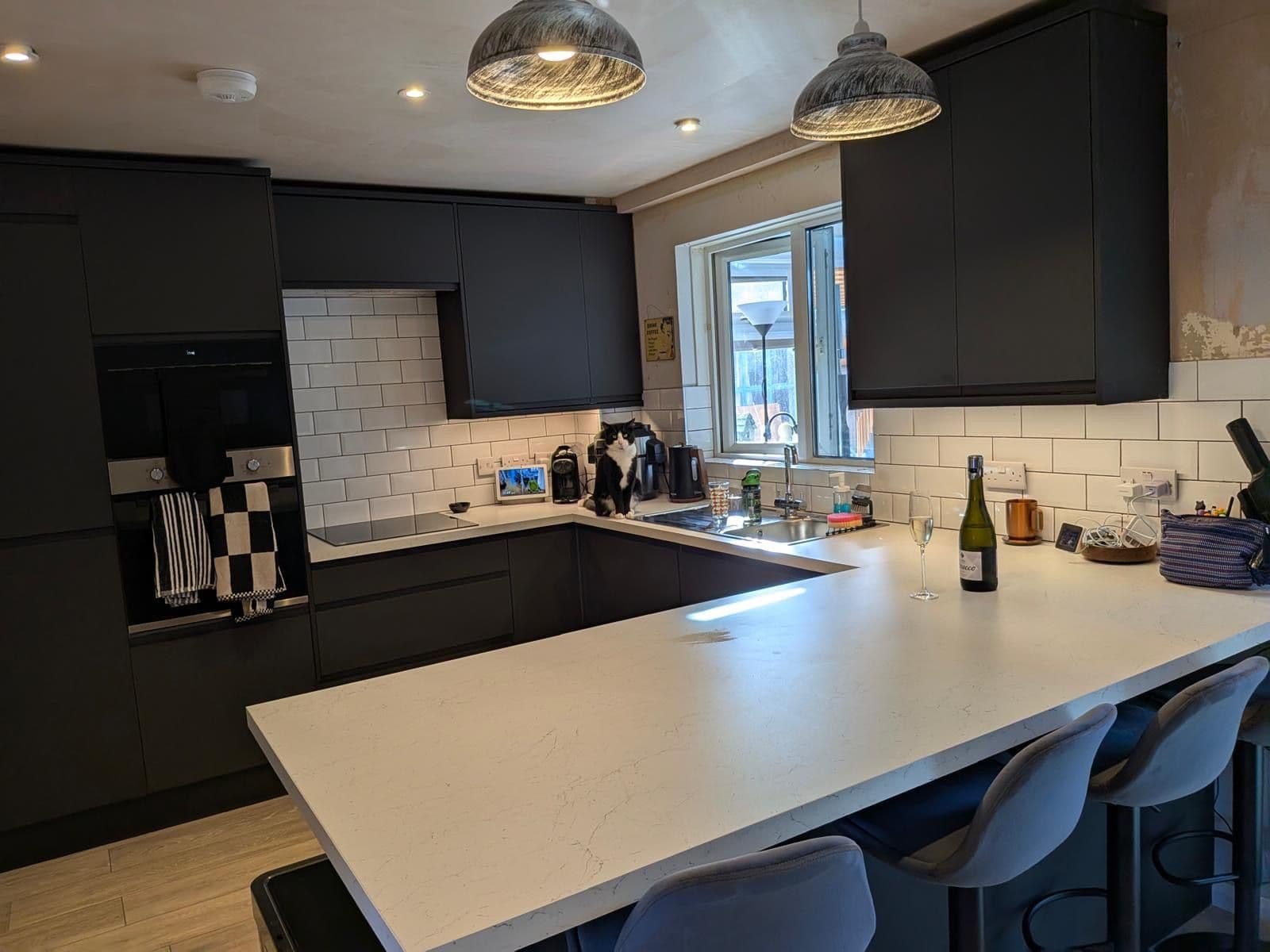 Black kitchen with white marble effect worktops, white metro tiled splashback and a cat sitting on the counter beside the hob