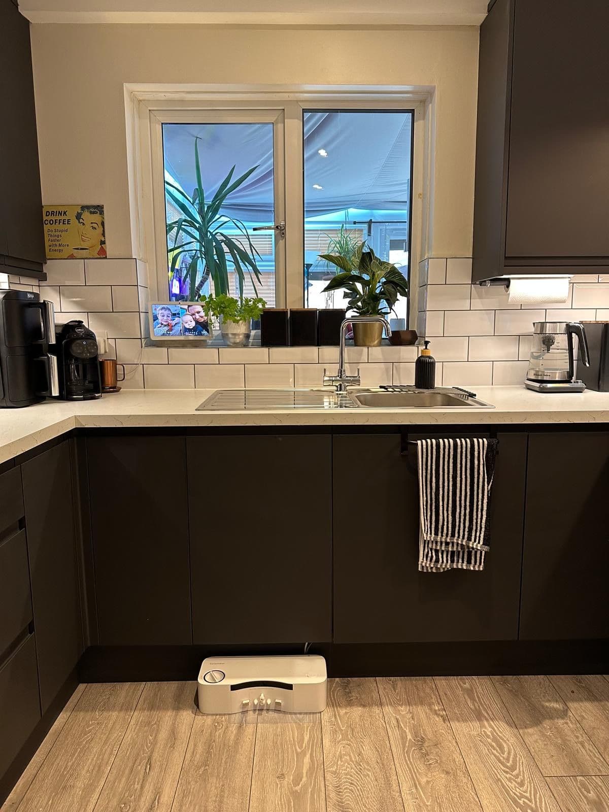 Kitchen sink area with a chrome mixer tap, white metro tiled splashback, window sill with house plants and a black kettle