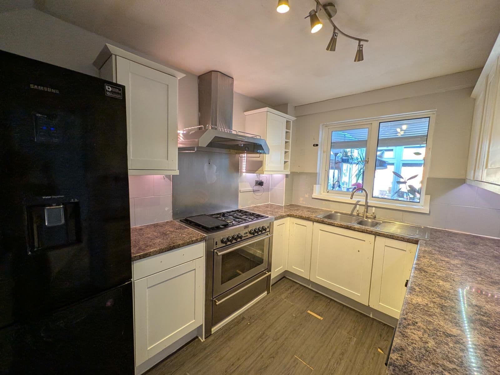 Original kitchen before renovation with white shaker style cabinets, a black fridge freezer, marbled laminate worktop and a freestanding gas range cooker