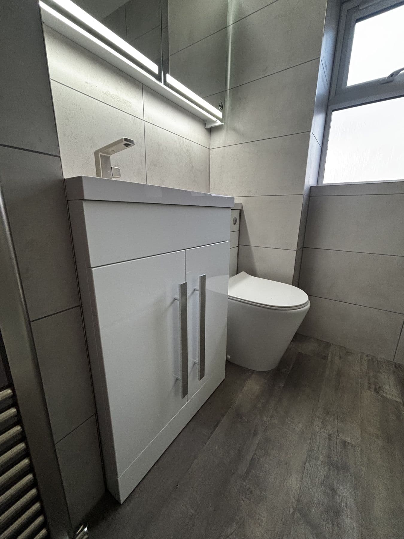 White vanity unit with gloss cabinet doors next to a wall hung toilet, under a frosted window