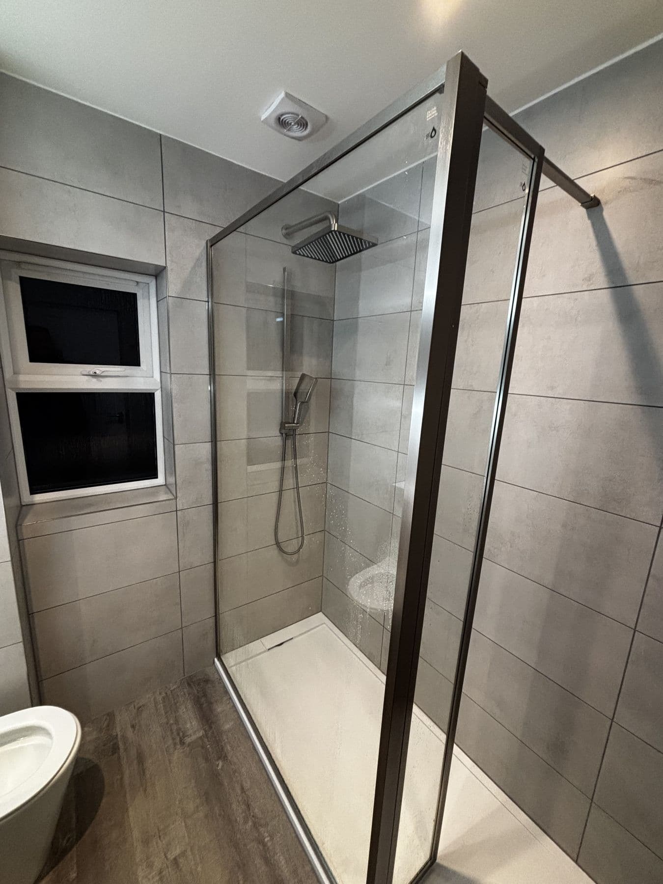 Walk in shower enclosure with a glass screen, rainfall shower head and handheld shower, toilet and frosted window behind