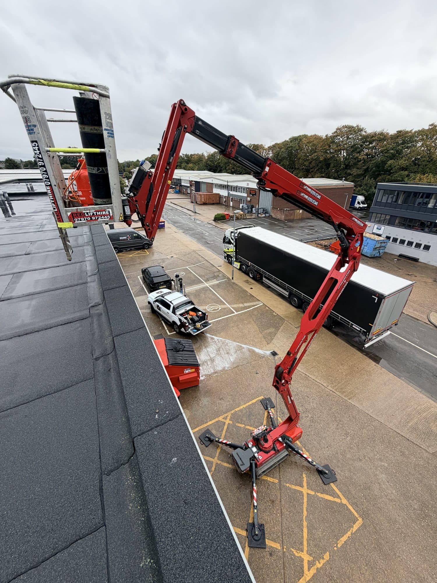 Another view of the cherry picker's articulated arm reaching up to the flat roof of the commercial unit