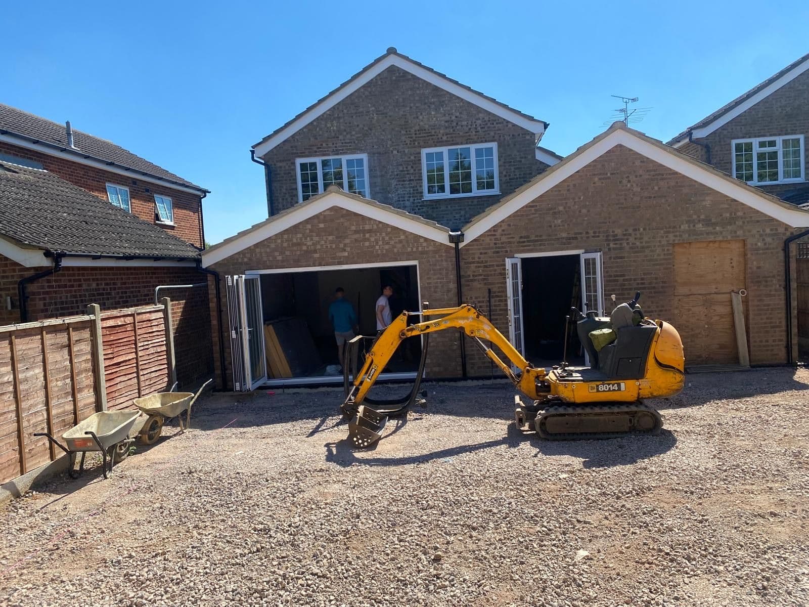 Rear extension under construction with bifold doors fitted, two workers inside and a mini digger on the cleared ground