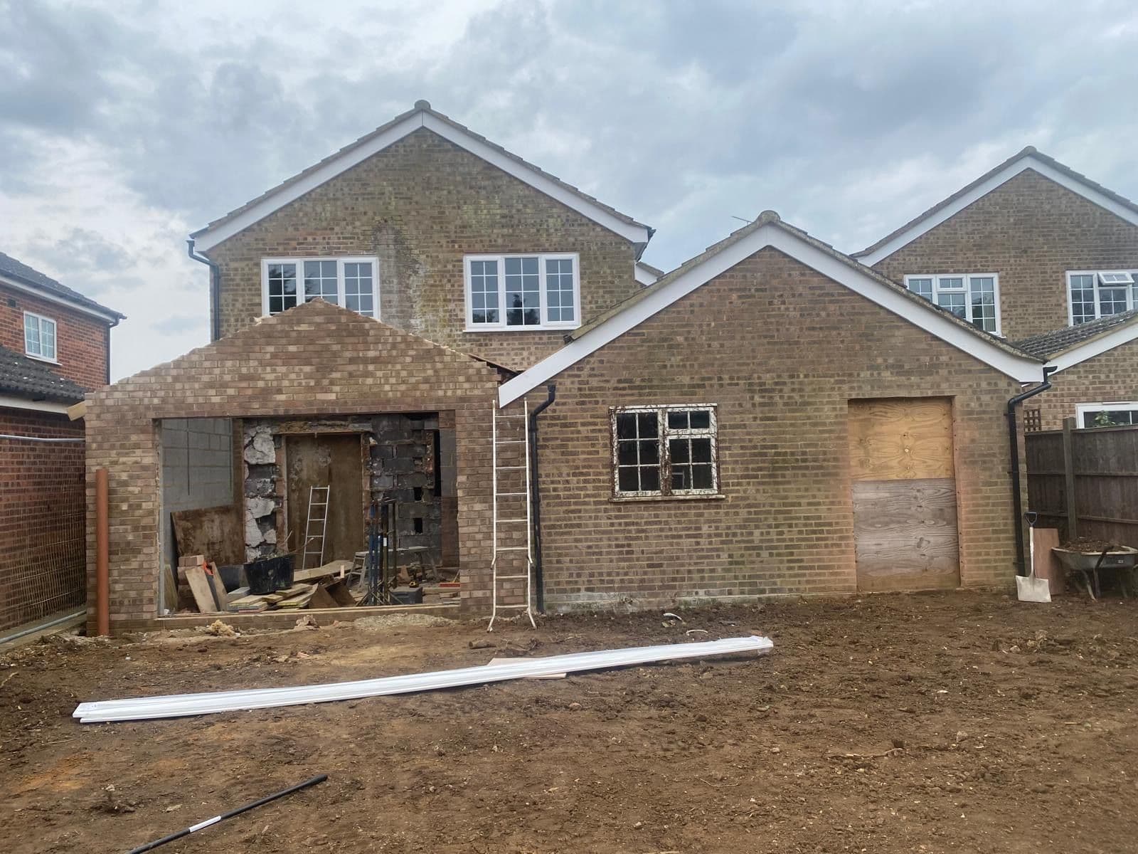 Rear extension under construction, brickwork shell with a boarded-up former garage opening and bare earth garden