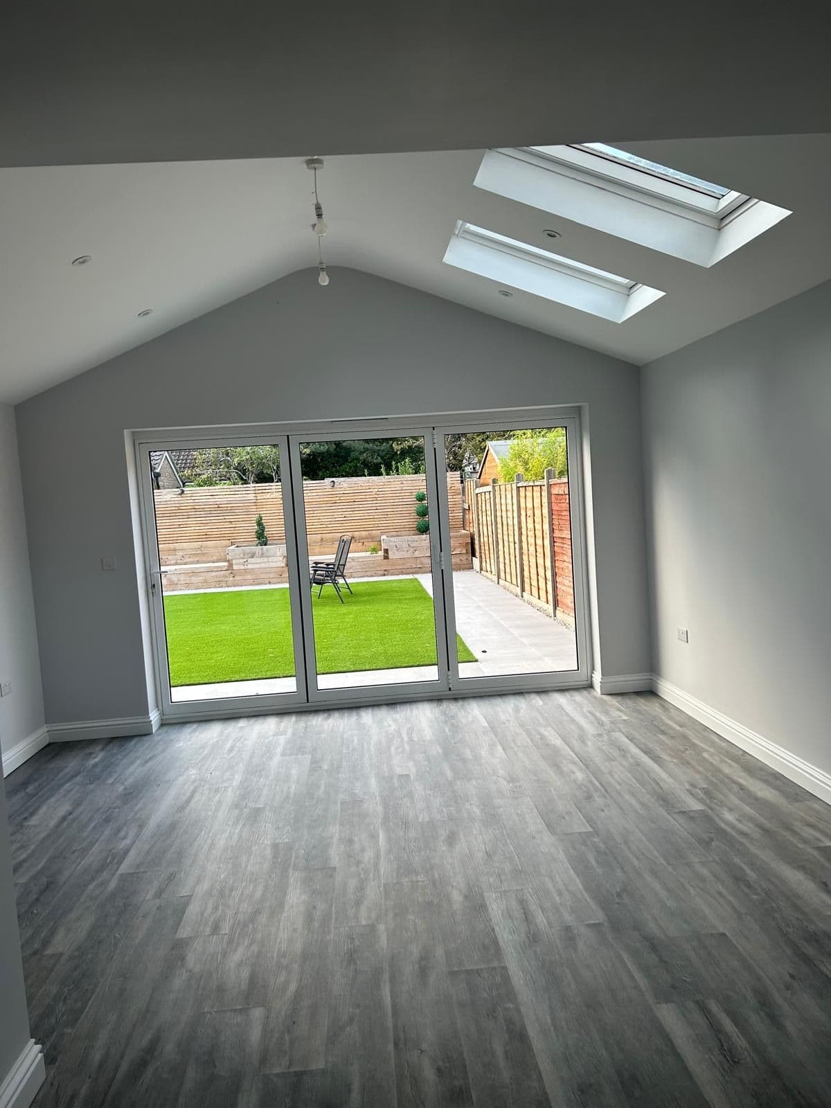 Open-plan extension with grey wood-effect flooring, vaulted ceiling with two skylights and bifold doors onto the garden