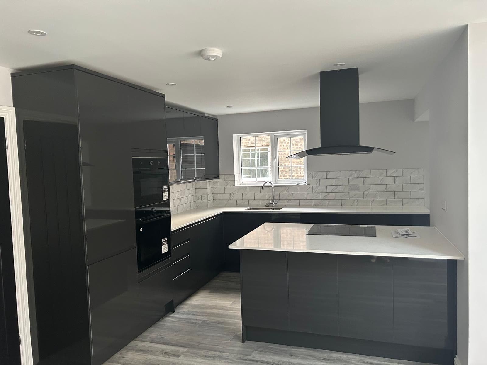 Dark grey gloss kitchen with white worktops, kitchen island, black extractor hood and marble-effect tiled splashback