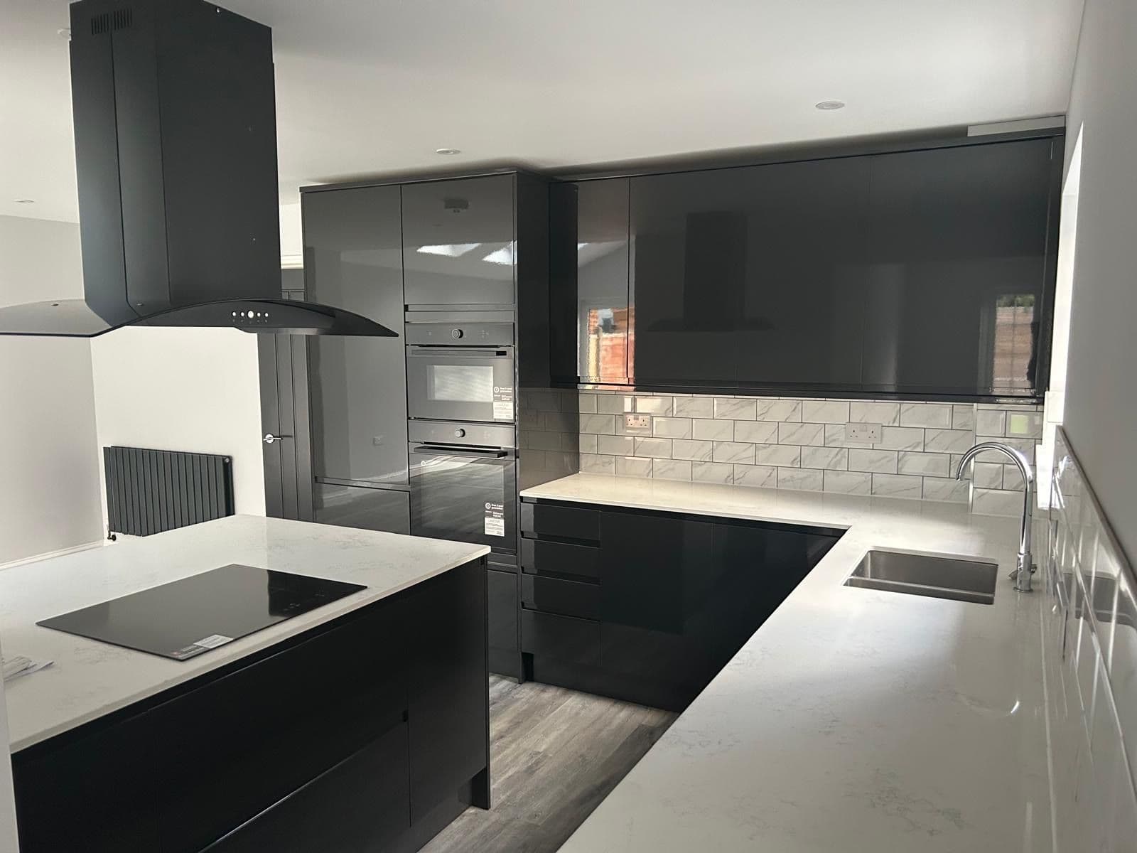 Dark grey gloss kitchen with black built-in ovens, induction hob on the island and white quartz worktops