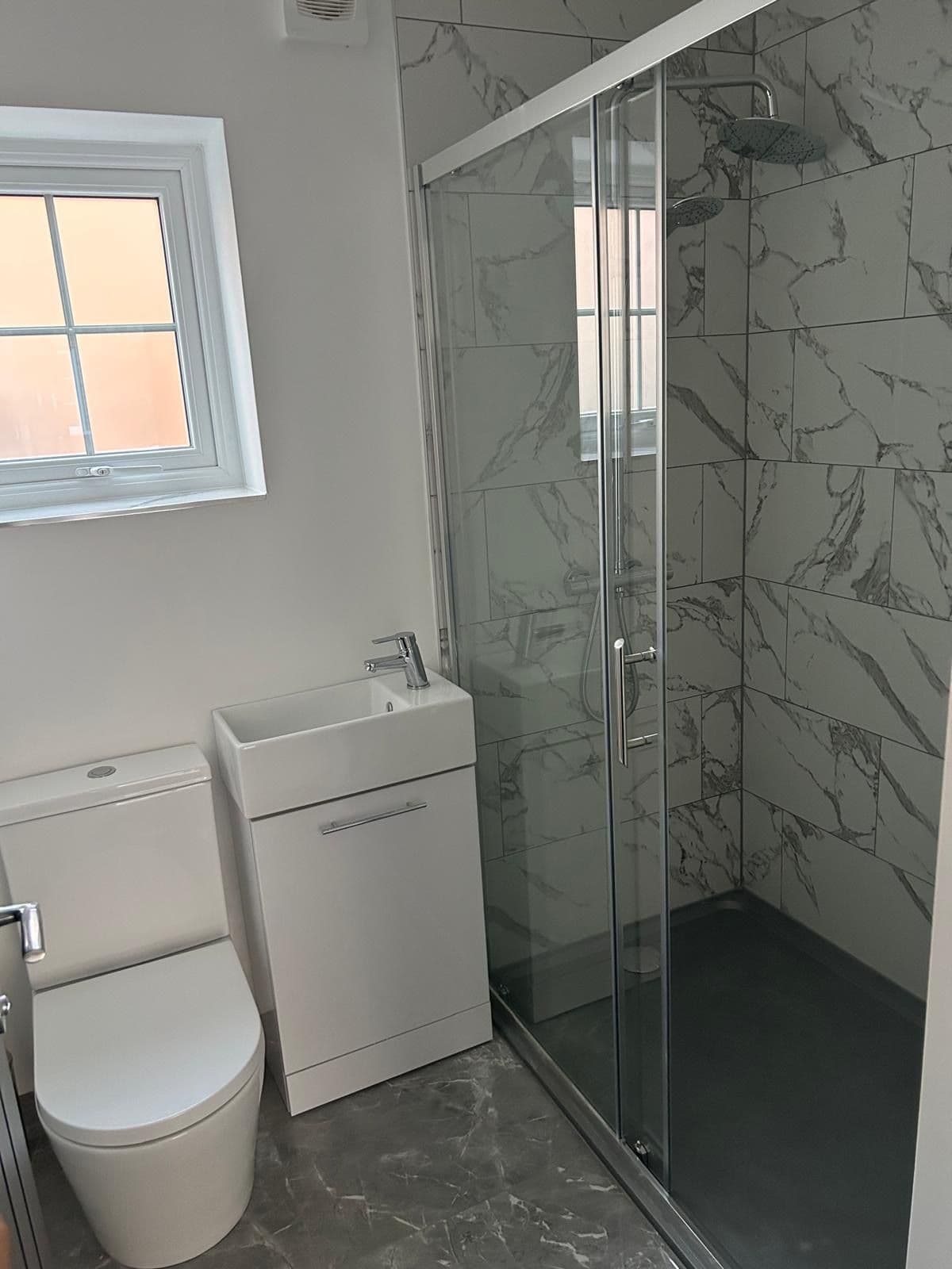 Compact bathroom with marble-effect tiled shower enclosure, small vanity basin and wall-hung toilet