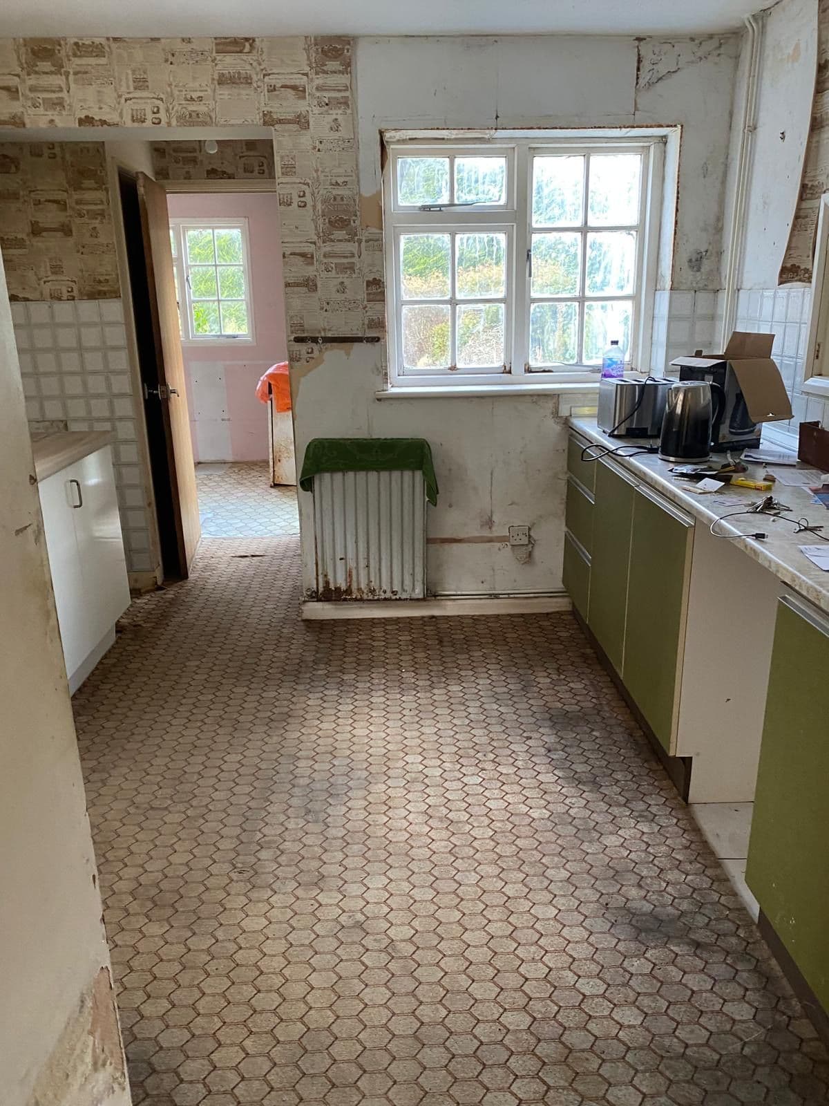 Original dated kitchen with green units, patterned lino flooring and peeling wallpaper before renovation